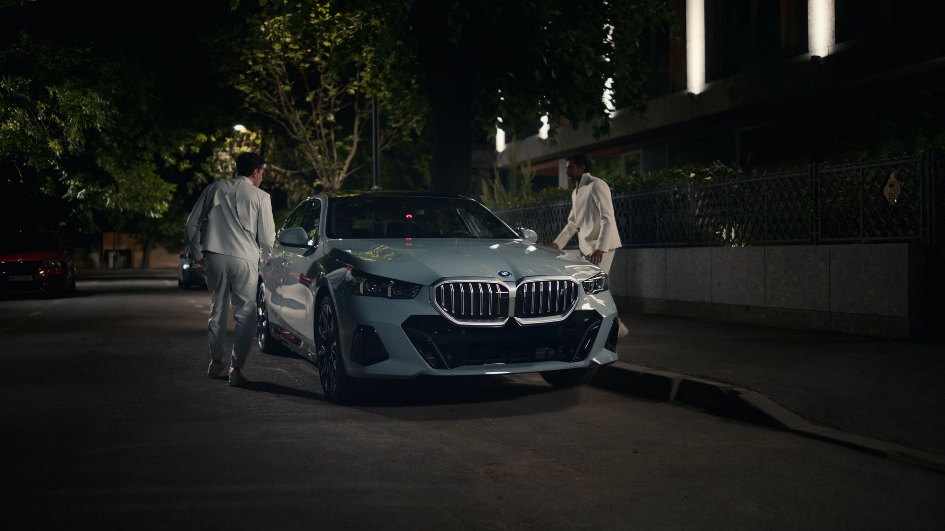 Two men approach a parked BMW at night